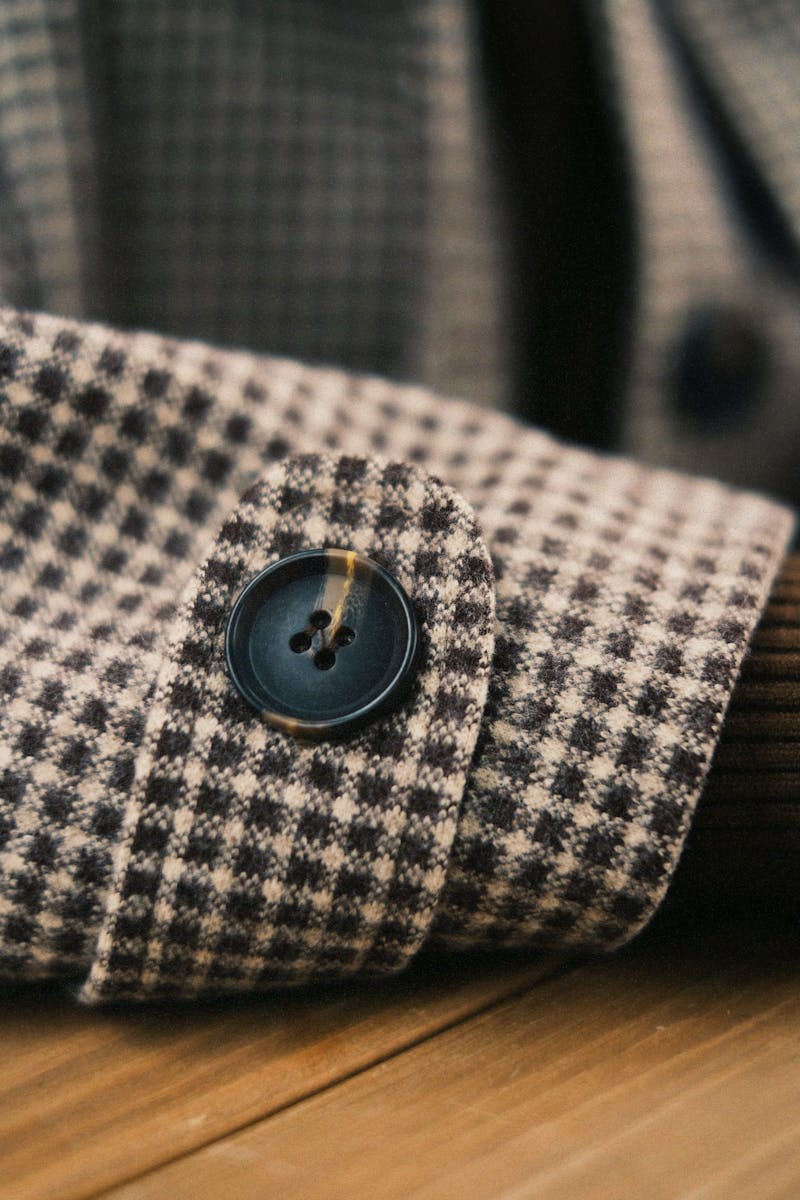 Detailed view of a checkered suit cuff with a black button, showcasing texture.